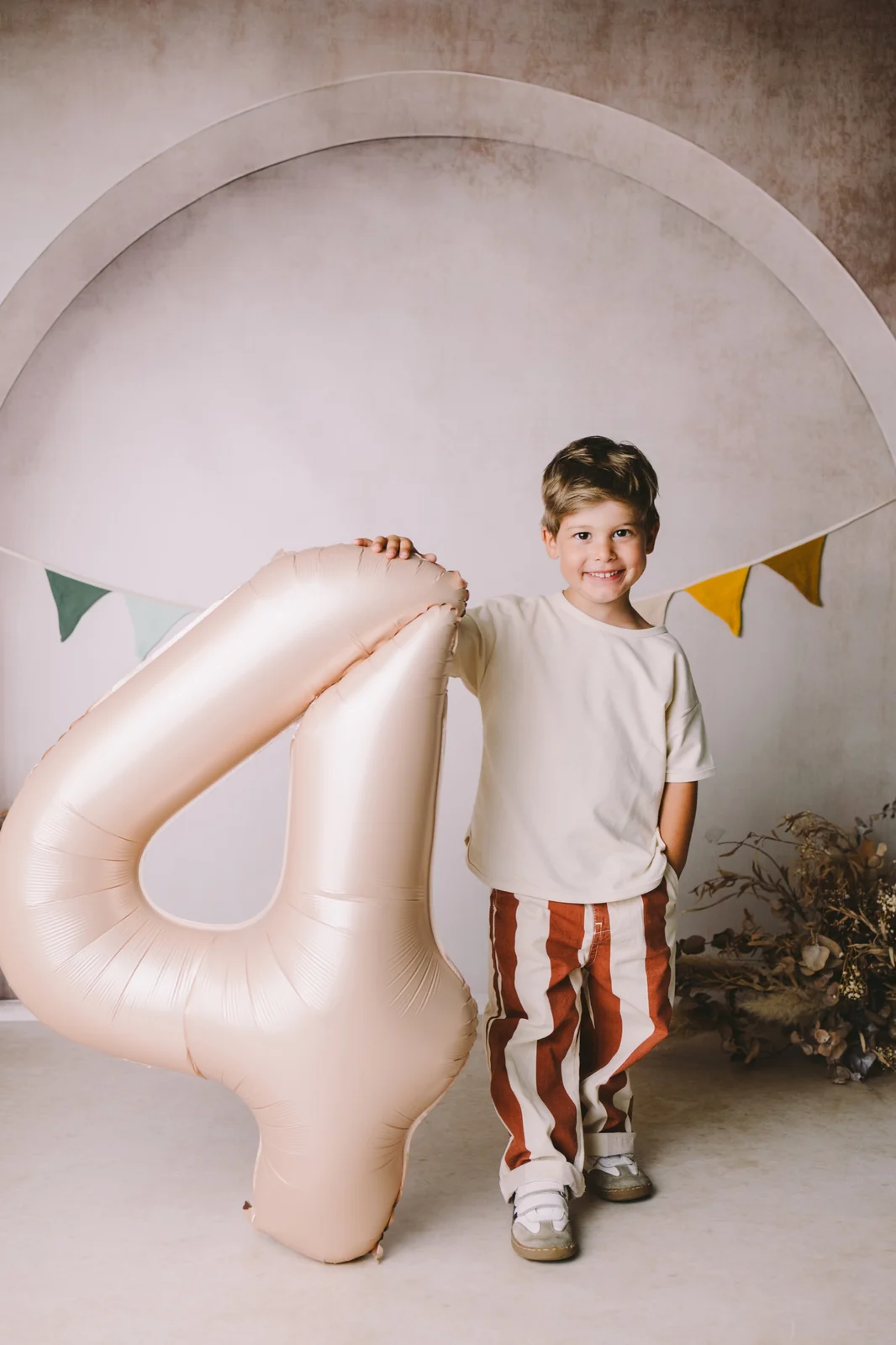 Sesión de cumpleaños en estudio en O Burgo, A Coruña — niño de pie junto a un globo con forma de número sobre fondo beige