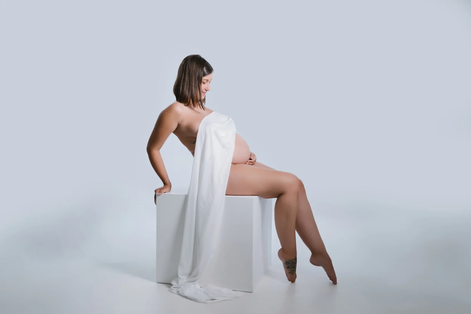 Sesión de embarazo en estudio en O Burgo, A Coruña — futura mamá sentada con una tela blanca sobre fondo claro