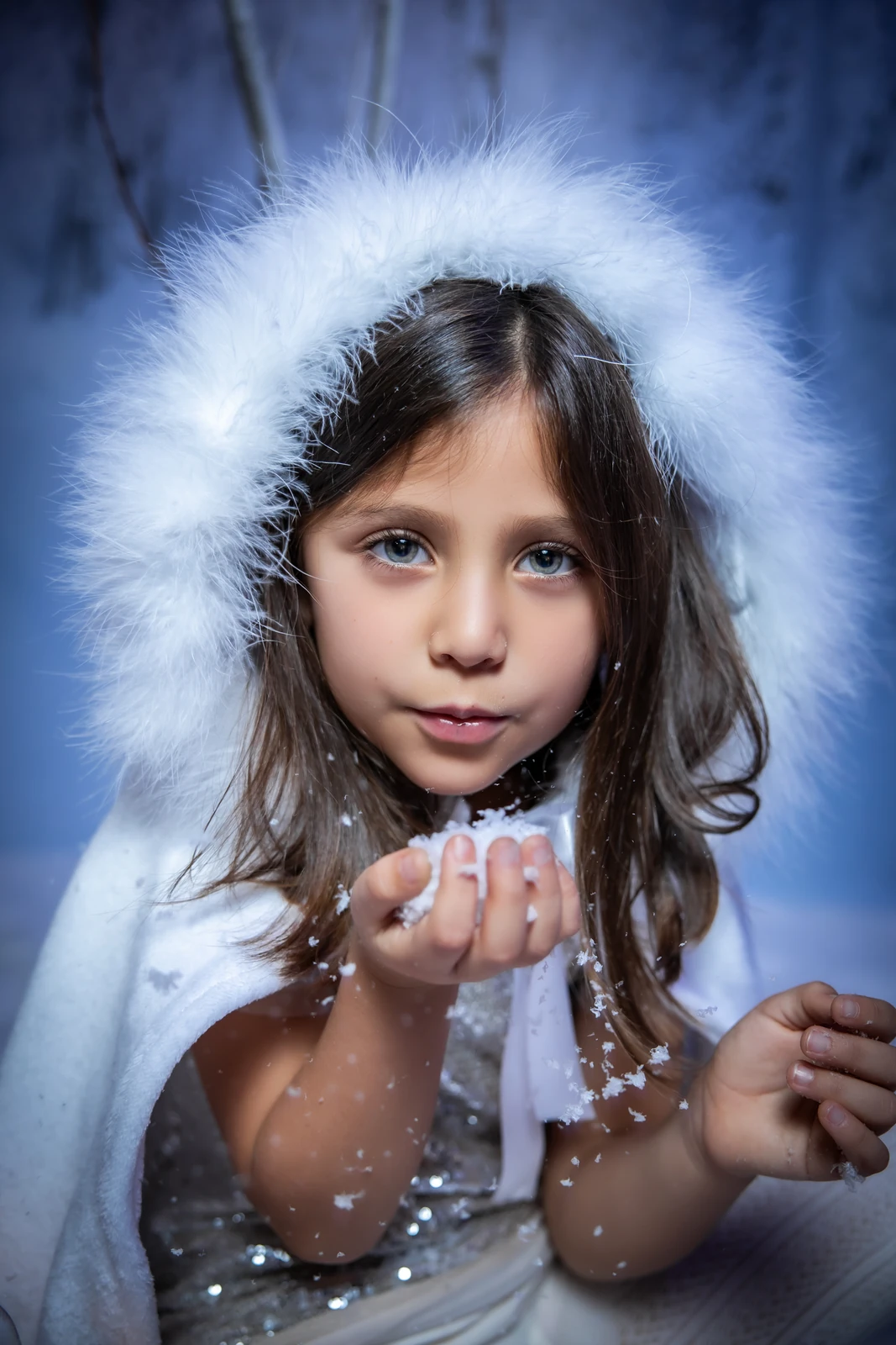Niña con capa blanca de pelo soplando nieve en una sesión de Navidad en el estudio de O Burgo