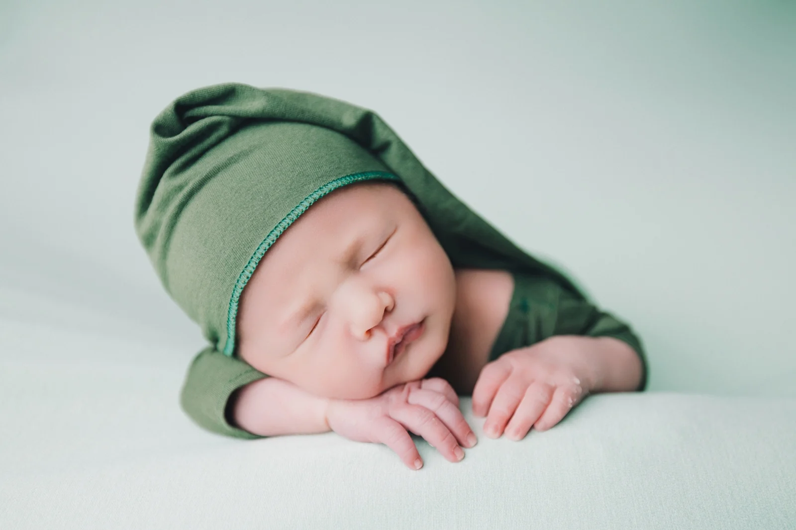 Bebé con gorro verde sobre fondo de tela, sesión newborn